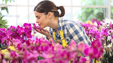 Woman in the garden of flowers, touches an orchid and smiling