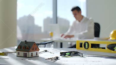 Young brunette architect sits by the table near a large window in white office construction company, He working on