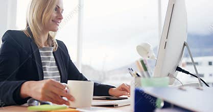 Businesswoman drinking cup of coffee while working on computer