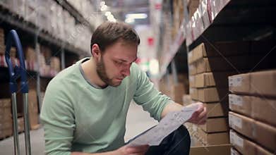 A man with a beard in a blue sweater checking his list in a warehouse
