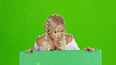 Bavarian girl looks out from behind the green board and winking. Green screen