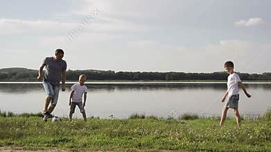 Father and two son playing football on the beach at the day time. Concept of friendly family.