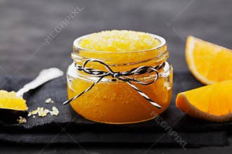 Orange body scrub with sugar and coconut oil in glass jar on black table. Homemade cosmetic for peeling and spa care