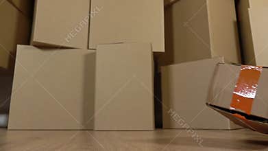Damaged parcel falling down on the floor. Brown cartons background. Flaw and unprofessional work concepts. Super slow