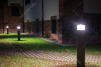Outdoor lights in front of an old building illuminating a walkway in the garden at night