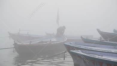 Man parking boat at foggy bay of river Ganges in Varanasi.