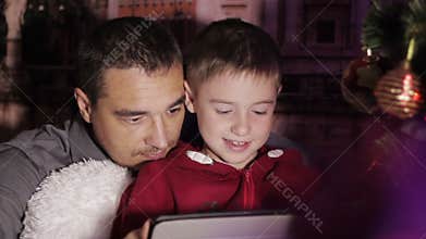 Father and son at the Christmas tree play on the tablet