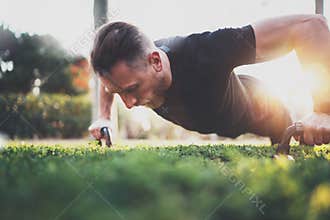 Muscular athlete exercising push up outside in sunny park. Fit shirtless male fitness model in crossfit exercise