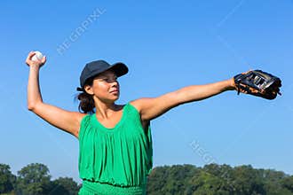 Woman with glove and cap throwing baseball outside
