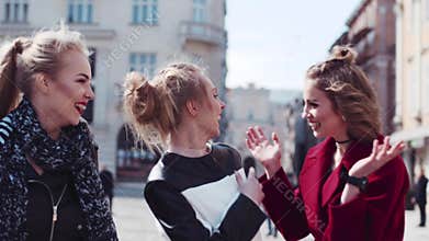 Happy three friends wandering in the old city center, laughing, and joking. The woman in a red coat hugs her friend
