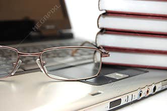 Eyeglasses and books on laptop