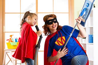 Preschooler girl and her mother dressed like superheroes. Middle-aged woman and kid playing while doing cleanup at home