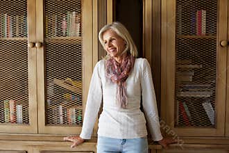 Beautiful older woman leaning against bookcase at home