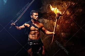 Fearless young muscular warrior with a torch in the dark