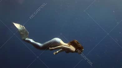 Young girl model underwater mermaid costume on blue background poses in Red Sea.