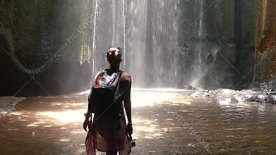 Young woman open arms to amazing waterfall in Bali
