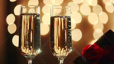 Two glasses filled with champagne and bokeh lights on the background