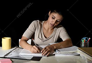 Young busy beautiful Spanish girl studying at home late night looking preparing exam writing on notepad
