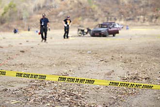 Police line tape with blurred law enforcement and wrecked car ba