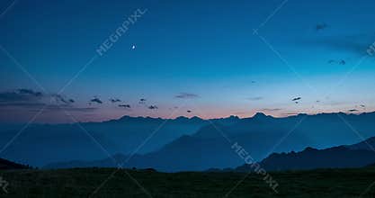 Day to night time lapse from high up on the Alps. Colorful sunset over mountain peaks and fog in the valleys below, moving clouds,