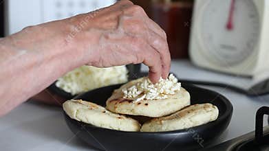 Woman adding shredded cheese to a roasted arepa