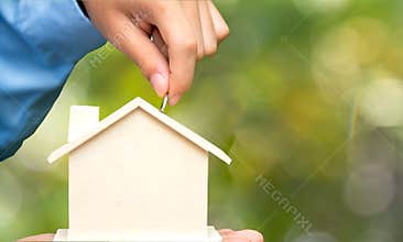 Male hand holding coins and piggy house bank save money, green nature background. Investment and save Concept.