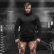 Muscular man with muscle legs in gym. Strong male in black hoodie with big quads