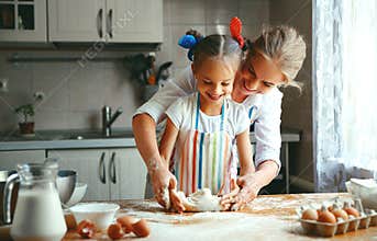 Happy family mother and daughter bake kneading dough in kitchen