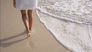 Woman legs leave footprints on the sand, wave washes away the footprints