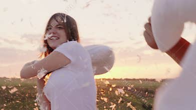 Young people are madly having fun. A woman is beating her pillow with a friend, feathers are flying. Fight against the