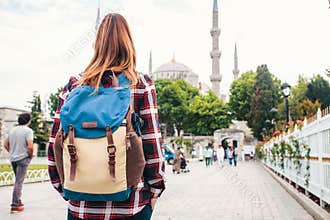 Young beautiful girl traveler with a backpack looking at a blue mosque - a famous tourist attraction of Istanbul. Travel