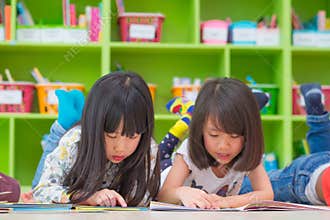 Two girl kid lay down on floor and reading tale book in prescho
