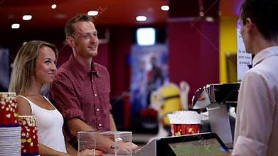 Excited young happy attractive guy girl couple making popcorn order from male cashier worker at cinema movie theater