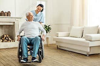 Cheerful positive caregiver moving a wheelchair