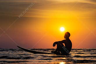 Silhouette of surf man sit on a surfboard. Surfing at sunset