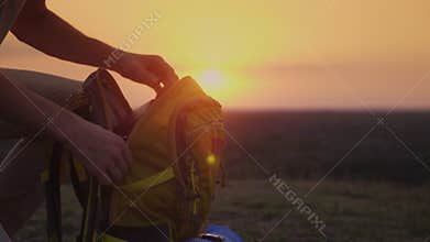 A man is packing his backpack at sunset. Preparing for a trip or trekking
