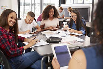 Teacher sitting with high school students using tablets