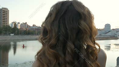 A beautiful girl in white clothes meets the dawn on the city embankment. Early morning, beautiful day.