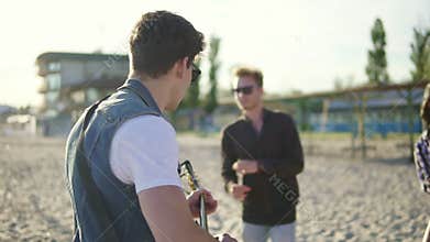 Summer party on the beach. Young friends drinking cocktails, dancing in the cirkle, playing guitar, singing songs and