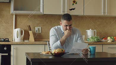 Slow motion of upset young man reading letter with unpaid bill in the kitchen at home