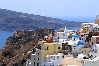 View on Santorini looking at colourful buildings dome churches with mountain and sea in the background.