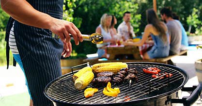 Mid section of man grilling corn, meat and vegetable on barbecue