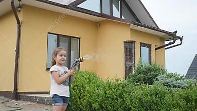 Cute little girl holding a water hose and shaking it as she waters the lawn