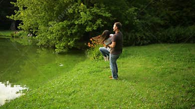 Happy couple is playing outside enjoying spending time together in the park. Strong boy whirls his girlfriend outdoors.