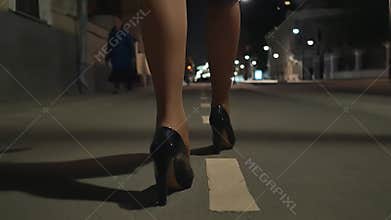 The legs of a young woman walking along the sidewalk of the night city.