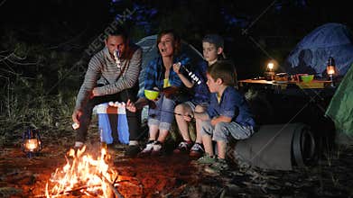 Parents with childs broil marshmallow on campfire to woodland, happy family fry marshmallow at fire