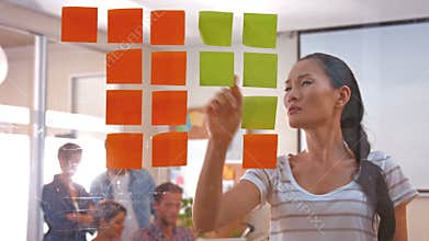 Casual businesswoman looking at post it with her colleagues behind