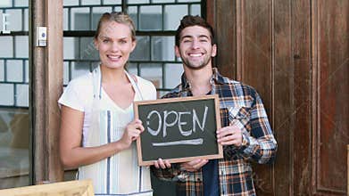 Smiling waitress and hipster man holding open signboard