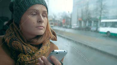 Woman using phone in bus on rainy day