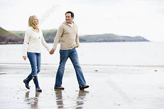 Couple walking on beach holding hands smiling